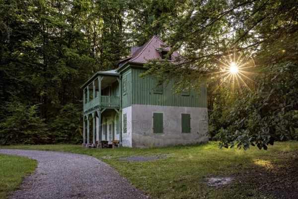Green house in the forest with evening sun, quiet path and wooden veranda in peaceful surroundings, The Riesenecke hunting complex in the Saale Holzland district in Thuringia