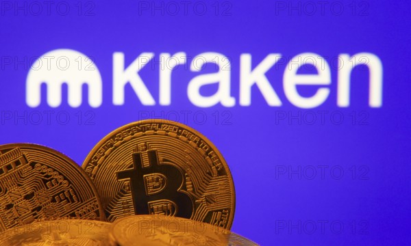 Dhaka, Bangladesh- 01 Nov 2025: Close-up of Bitcoin coins with the Kraken logo visible on a screen in the background