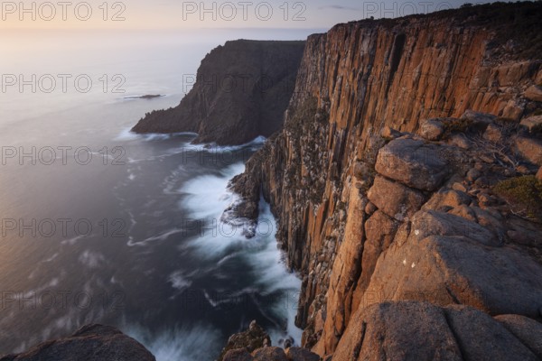 Long exposure shows sunset over the cliffs of Cape Raoul. Golden light hits the sea and colors the rocks warmly in the evening. Cape Raoul, Tasman Peninsula, Tasmania, Australia