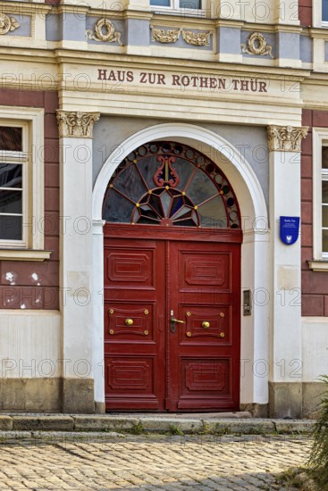 Red door in a historic building with decorative stone elements and symmetrical decorations, door to the Red Door House in the old town of Arnstadt in Thuringia
