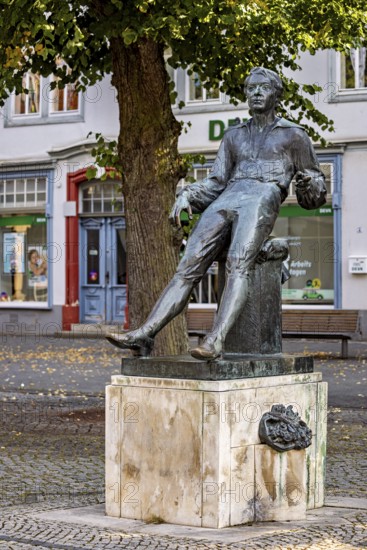 Seated bronze statue of a man under a tree in a city, Johann Sebastian Bach monument in the old town of Arnstadt in Thuringia