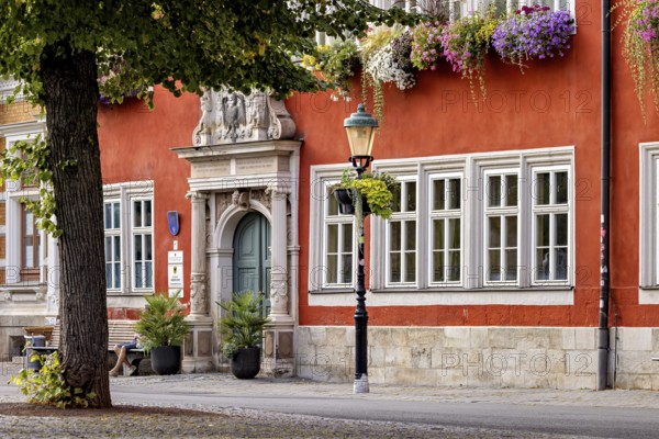 Red façade with blooming flowers and lantern next to an ornate entrance in the old town, The old town of Arnstadt in Thuringia