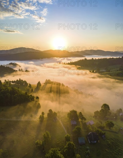 Sunrise over a fog covered village in a rural landscape, golden morning light, serene autumn atmosphere, hills and mountains in the background, AI generated
