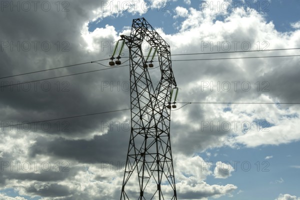 High voltage power lines against a bright blue sky with scattered clouds, Puy de Dome, Auvergne Rhone Alpes, France