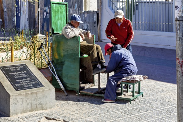 Three men interact in a relaxed street scene at a shoe shiner in the old town, show shiners in the town of Uyuni in the Salar de Uyuni in Bolivia