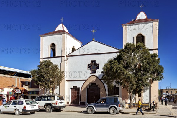Church with two towers and cross in a busy street, surrounded by cars and people under a clear blue sky, church in the city of Uyuni in the Salar de Uyuni Bolivia