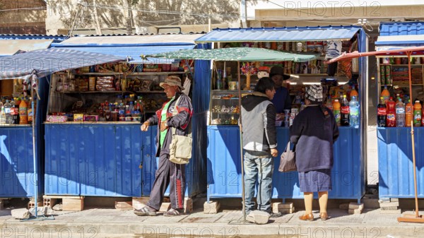 Street market with a blue stall, people buy colourful bottles and products under a blue sky, small shops in the town of Uyuni in the Salar de Uyuni in Bolivia