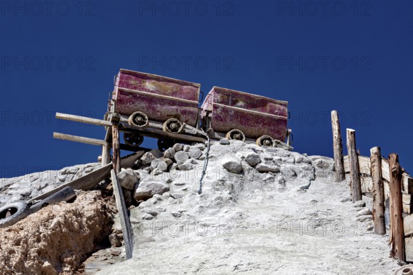 Two old mine cars standing on a rocky structure above a stony slope under a clear sky, mining lore at the Cerro Rico silver mountain near Potosi Bolivia