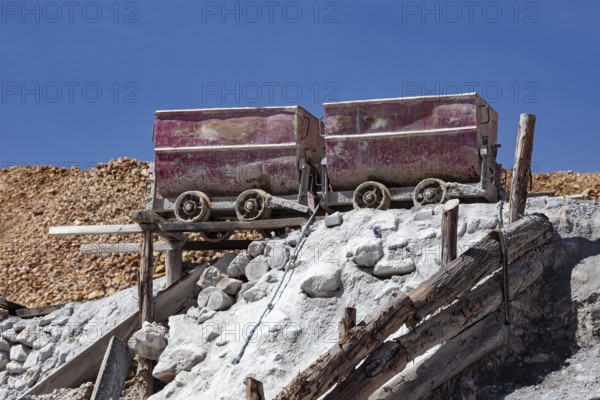 Two rusty mine cars on a wooden scaffold, surrounded by piles of rocks in a sunny mining environment, mining lore at the Cerro Rico silver mine near Potosi Bolivia