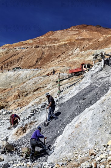 A worker shovels stones down a hill, accompanied by an arid landscape, The silver mines of Potosi Bolivia
