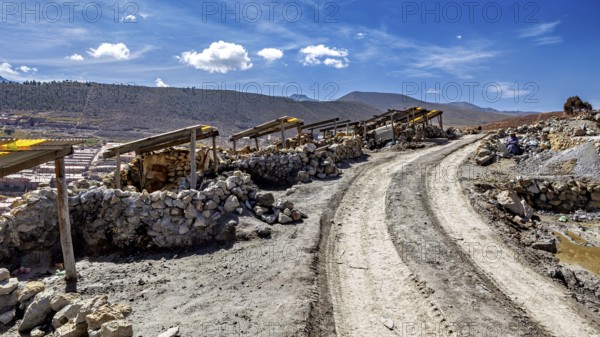 Dusty path with piles of stones next to a mountainous landscape under a blue sky with clouds, The silver mines of Potosi Bolivia