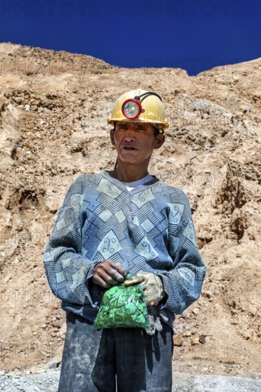 A man in a helmet and patterned jumper stands in front of a rocky landscape, The miners of the Cerro Rico silver mountain near Potosi Bolivia