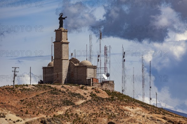 A hill with a large statue and several radio towers against a cloudy sky, The church on the Cerro Rico silver mountain near Potosi in Bolivia