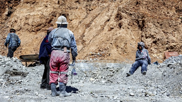 Miners in different clothes stand or sit in a barren, dusty environment, The miners of the Cerro Rico silver mountain near Potosi Bolivia