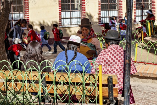 Women in traditional dress sit in the park while children play, people of the town of Uyuni in the Salar de Uyuni in Bolivia