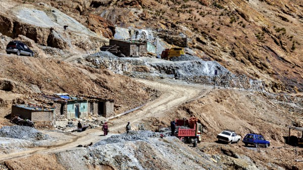 Stone houses on a dirt road with passing cars and mining scenes, The silver mines of Potosi Bolivia