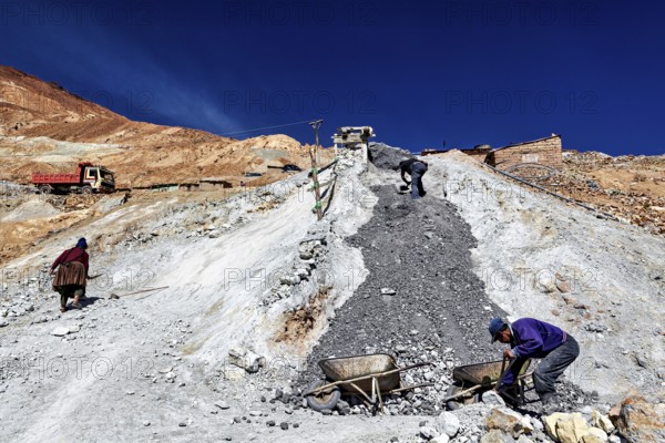 Workers with wheelbarrows on a stony slope under a bright blue sky, The silver mines of Potosi Bolivia