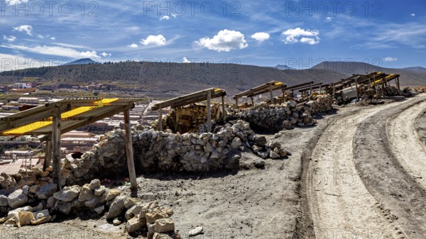 A dirt track leads through a dry, stony landscape under a blue sky with clouds, The silver mines of Potosi Bolivia