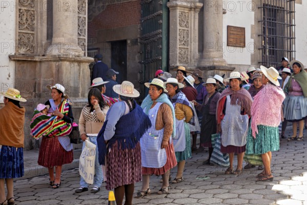 Women in traditional dress stand on a busy cobbled street in front of a historic building, demonstration in the streets of Potosi Bolivia