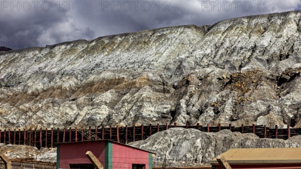 Industrial landscape with buildings at the foot of steep rock faces under a cloudy sky, slag heap of the silver mines in Potosi Bolivia