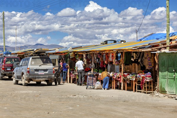 Various market stalls with visitors and cars, lively rural atmosphere under a cloudy sky, market stall for tourists in the Salar de Uyuni in Bolivia