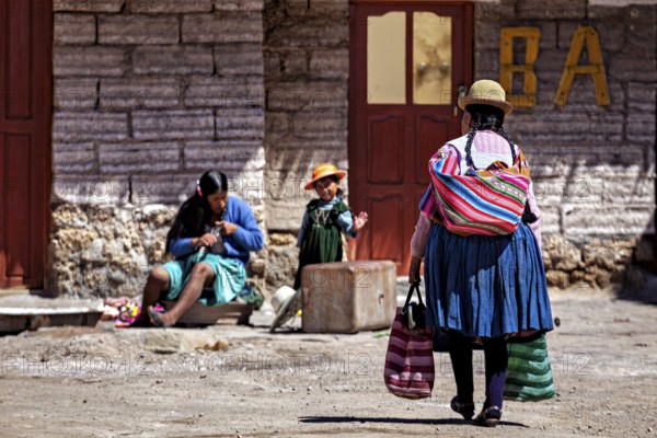 A woman approaches a small group in which a child is playing and another woman is sitting, Traditional woman in a village in the Salar de Uyuni in Bolivia