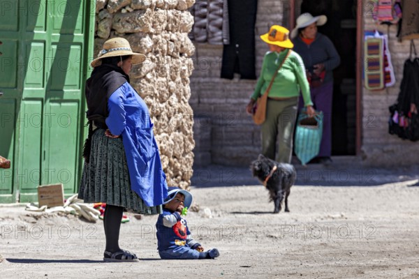 Woman and child in traditional dress stand with a dog in front of a green door in the village, Traditional woman in a village in the Salar de Uyuni in Bolivia
