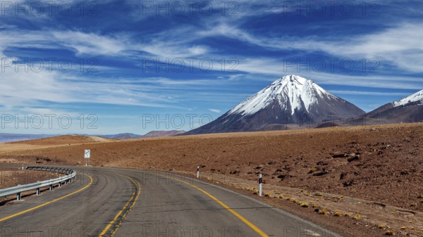 Deserted road leads to a snow-covered mountain under a clear sky, The landscape with the volcanoes on the Altiplano in Bolivia