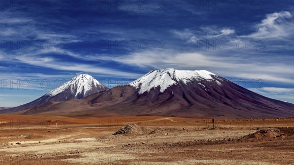 Two snow-capped mountains under a clear sky in a dry landscape, The landscape with the volcanoes on the Altiplano in Bolivia