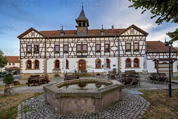 Half-timbered building with fountain and seating on cobblestone square at dusk, Historic half-timbered house in the village of Mühlburg in Thuringia near Erfurt