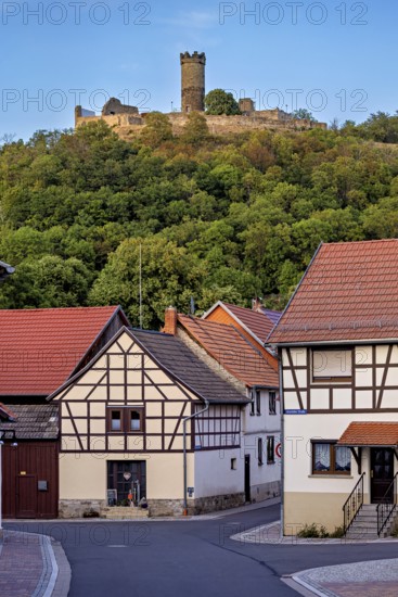 A village with half-timbered houses and a hill with a castle in the background, the ruin Mühlburg one of the Drei Gleichen near Erfurt in Thuringia