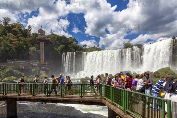 Tourists on a bridge watch the impressive waterfalls in the background, The Iguazu Falls between Argentina and Brazil