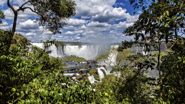 Lush green surroundings, waterfalls in the background, viewpoint with visitors, The Iguazu Falls between Argentina and Brazil