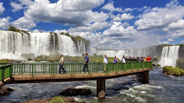 People walk on a bridge in front of an impressive waterfall under a blue sky, The Iguazu Falls between Argentina and Brazil