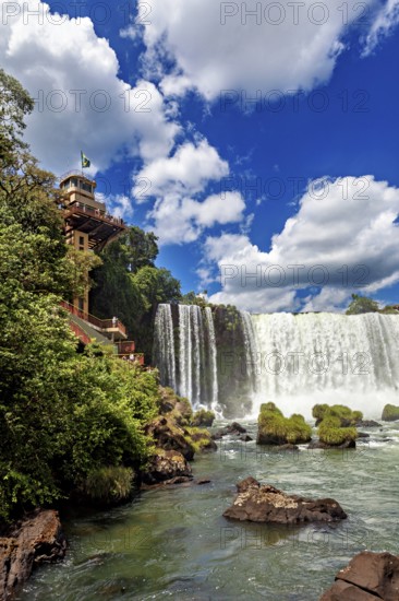 Impressive waterfall with neighbouring building and flag, blue sky and lush greenery, The Iguazu Falls between Argentina and Brazil