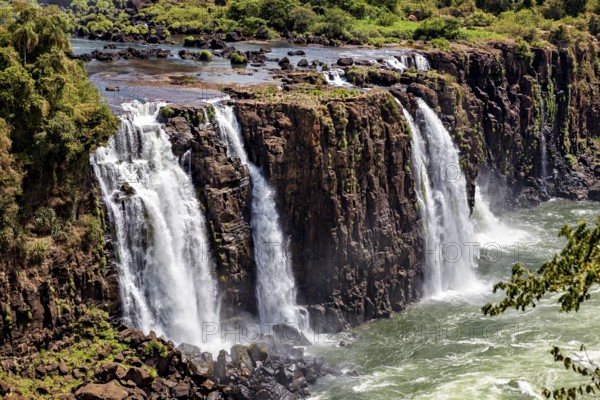 Wide waterfalls cascade over steep cliffs into a bubbling river, The Iguazu Falls between Argentina and Brazil