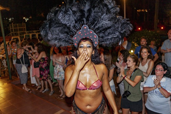 Woman in exotic costume with feather headdress gives kisses to the crowd, samba dancers to entertain tourists at the waterfalls of Iguazu in Argentina