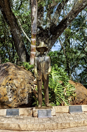Bronze statue of a man with a hat and suit, surrounded by trees and rocks in a natural setting, Statue of Frederico Engel at the waterfalls of Iguazu in Argentina