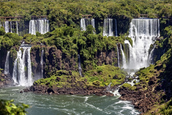 Various waterfalls flow over rocky cliffs, embedded in a lush green landscape, The Iguazu Falls between Argentina and Brazil