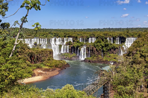 Panorama of the waterfalls with walkway along the river and dense deciduous forest, The Iguazu Falls between Argentina and Brazil