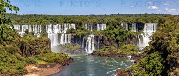 An impressive panoramic view of a cascade of waterfalls flanked by lush greenery and a clear sky, The Iguazu Falls between Argentina and Brazil