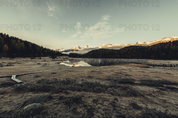 Lake Staz near Sankt Moritz in the Engadin in Switzerland. Morning atmosphere with fog in autumn. Water reflection and snow-covered mountains in the background