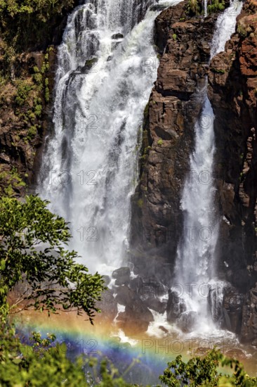 Large waterfall surrounded by rocks with a rainbow nearby, surrounded by forest, The Iguazu Falls between Argentina and Brazil