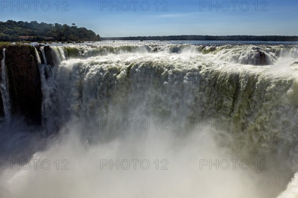 A mighty waterfall with rising spray under a clear blue sky, The Iguazu Falls between Argentina and Brazil
