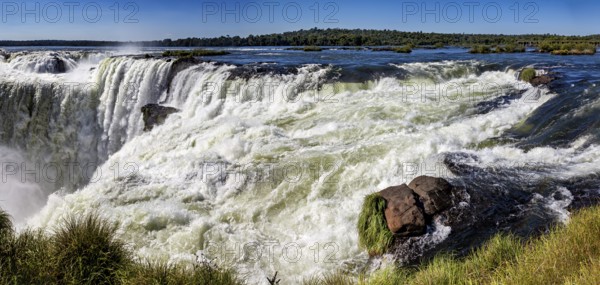 Panoramic view of the raging river and waterfall, surrounded by rocks and lush greenery, The Iguazu Falls between Argentina and Brazil