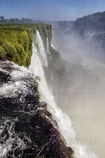 Majestic view of the waterfall, surrounded by green grass and rising mist, The Iguazu Falls between Argentina and Brazil