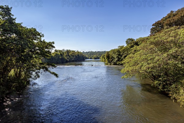 A calm river flows through a forested landscape under a clear blue sky, The Iguazu River between Argentina and Brazil