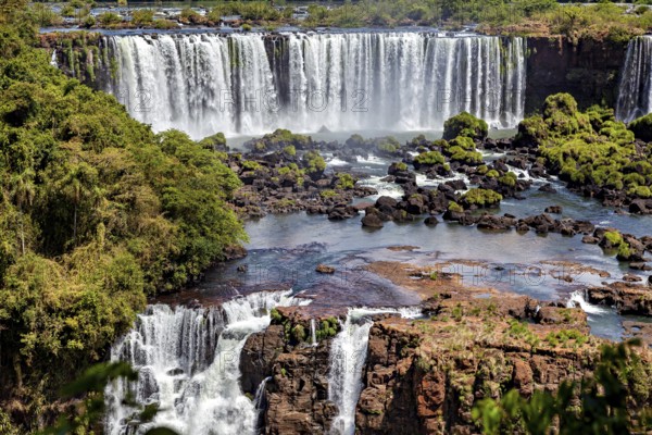 Waterfalls cascade over rocks into a wide river surrounded by dense forest, The Iguazu Falls between Argentina and Brazil