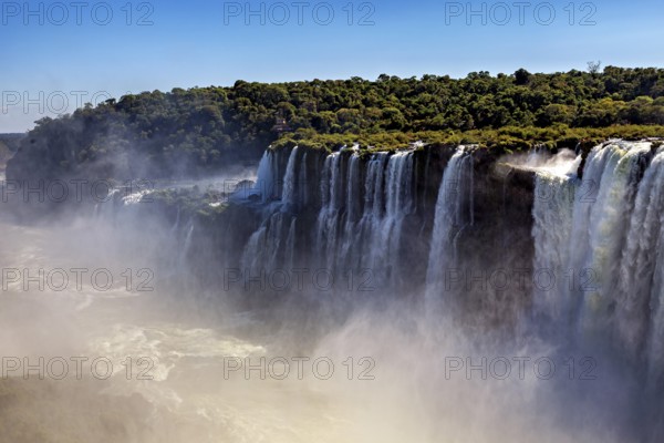 Row of waterfalls creates mist over green cliffs and conveys a peaceful atmosphere, The Iguazu Falls between Argentina and Brazil