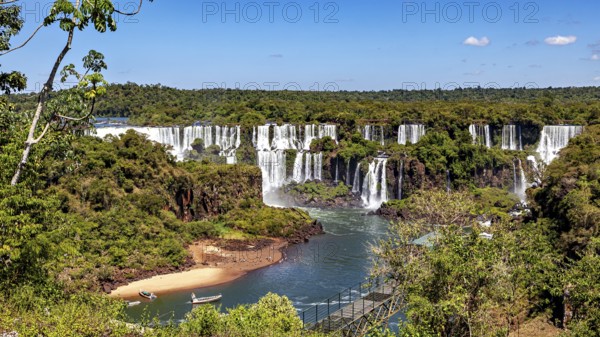 Picturesque waterfalls with a small beach on the left under a clear sky, The Iguazu Falls between Argentina and Brazil